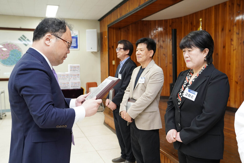 정장을 입고 안경을 낀 남성이 검은색 캐쥬얼 자켓을 입은 고화순에게 패를 수여하고 있다
