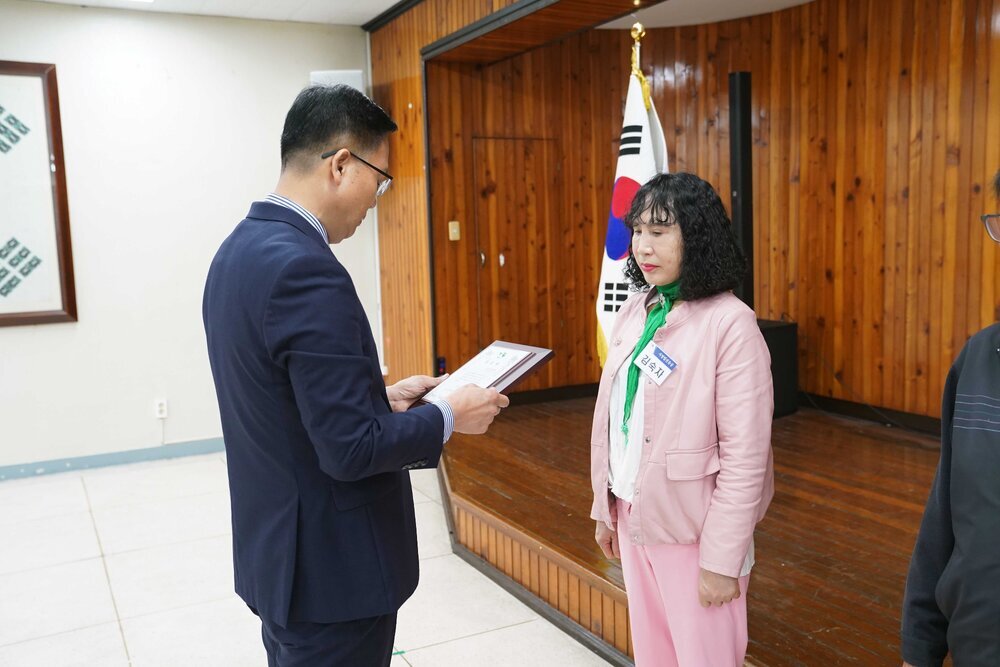 4월 정례조회에 정장을 입고 안경을 낀 남성이 위아래 분홍색 자켓과 바지를 입은 김숙자에게 패를 수여하고 있다