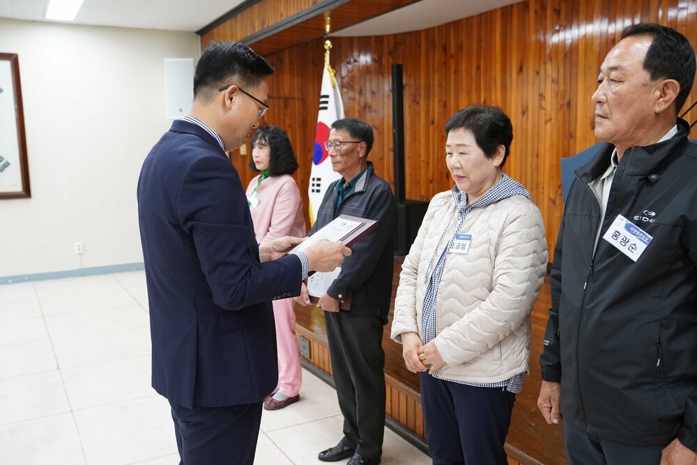 4월 정례조회에 정장을 입고 안경을 낀 남성이 밝은 베이지색 패딩을 입은 조금임에게 패를 수여하고 있다