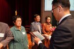정장 차림의 관계자가 녹색 상의를 입은 여성 수상자에게 패를 전달하며 읽고 있는 모습이다.
