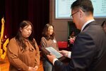 정장 차림의 관계자가 갈색 블라우스를 입은 여성 수상자에게 패를 전달하며 읽고 있는 모습이다.